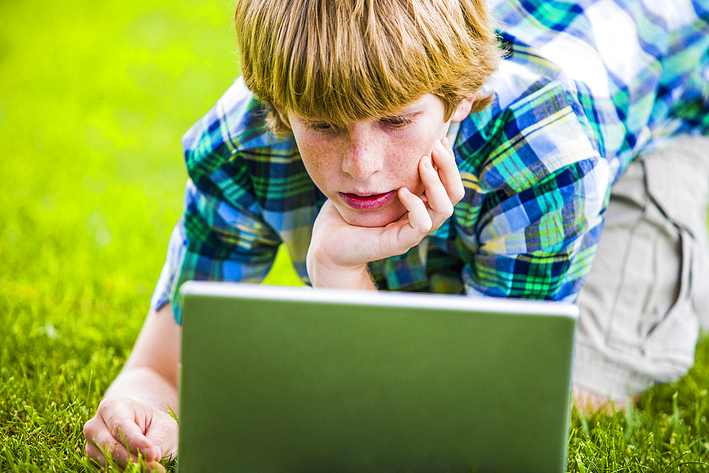 Caucasian boy kneeling in grass using laptop