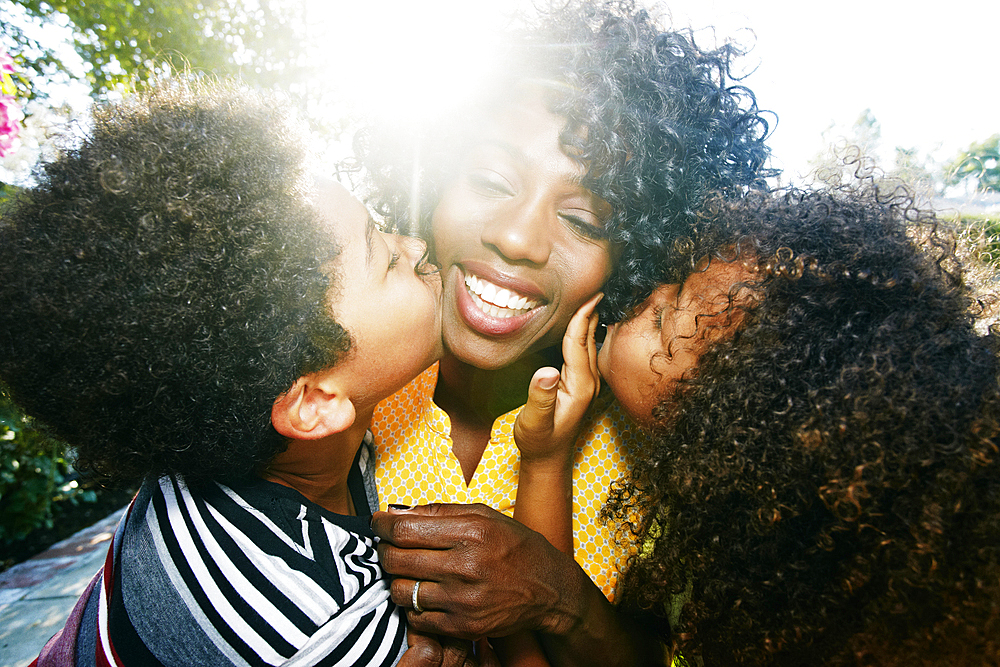 Son and daughter kissing cheeks of mother outdoors