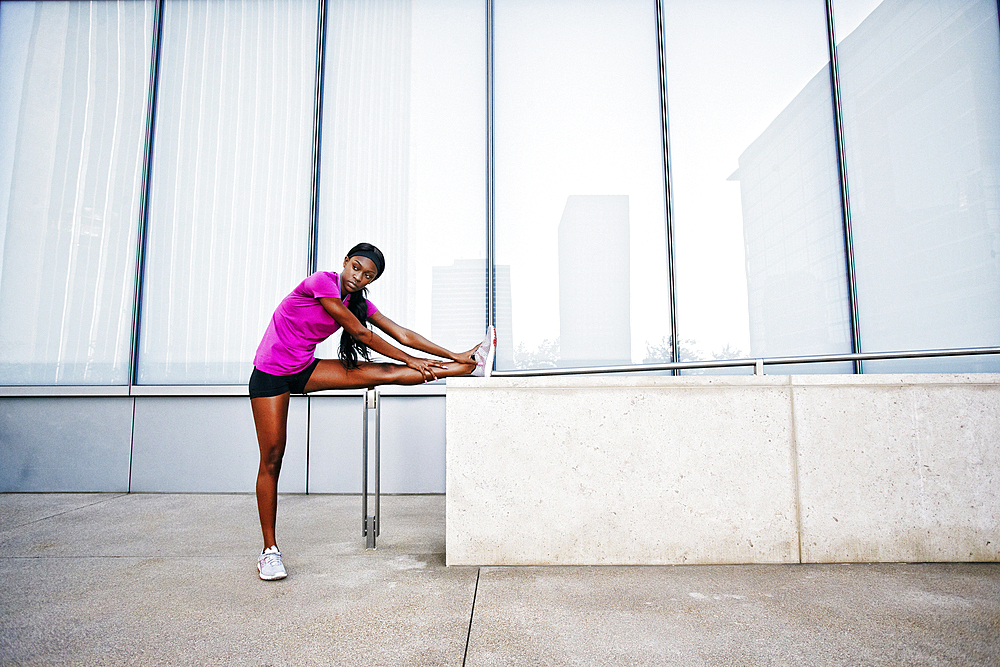 Black woman stretching leg on urban wall