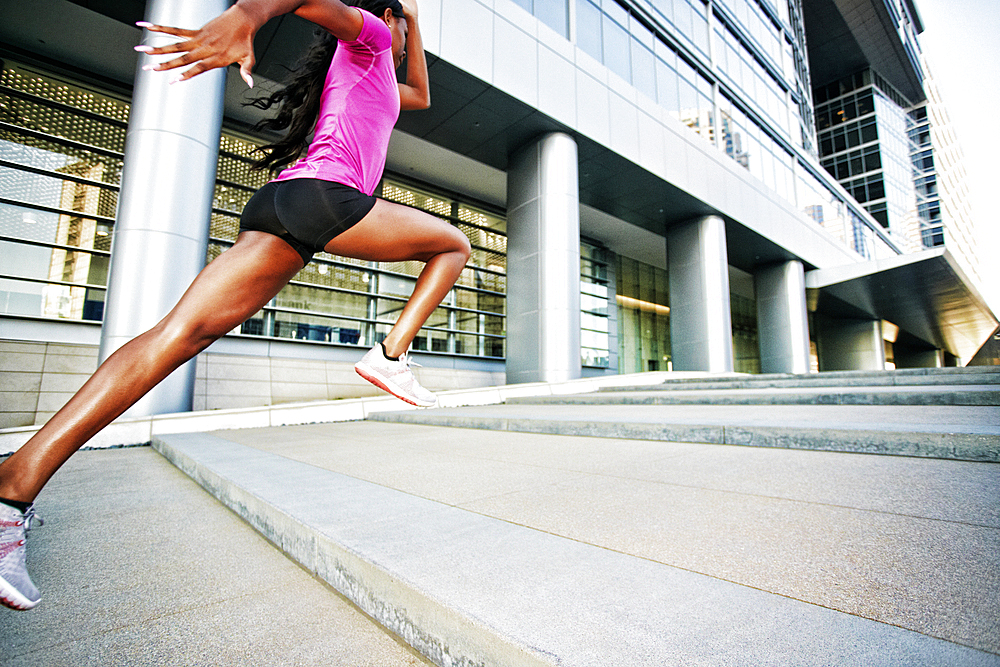 Black woman running and jumping on city staircase