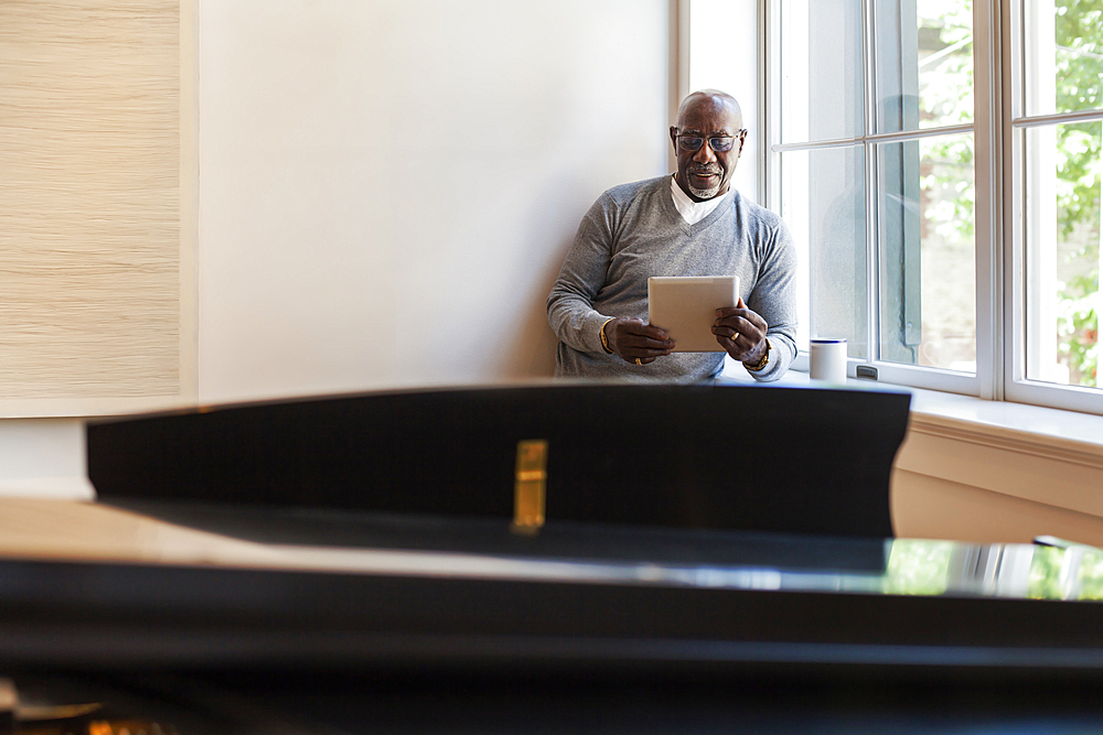 Man using digital tablet near window behind piano