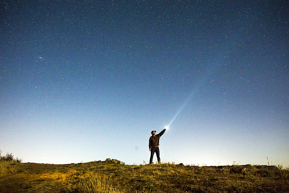 Caucasian man pointing flashlight at night sky