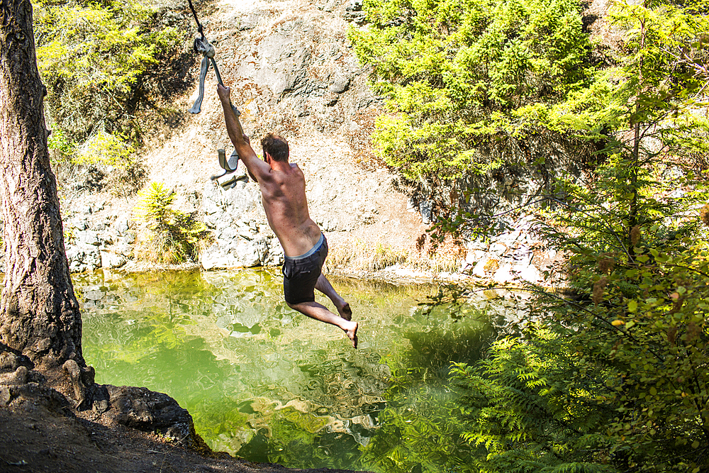 Caucasian man swinging on rope over water