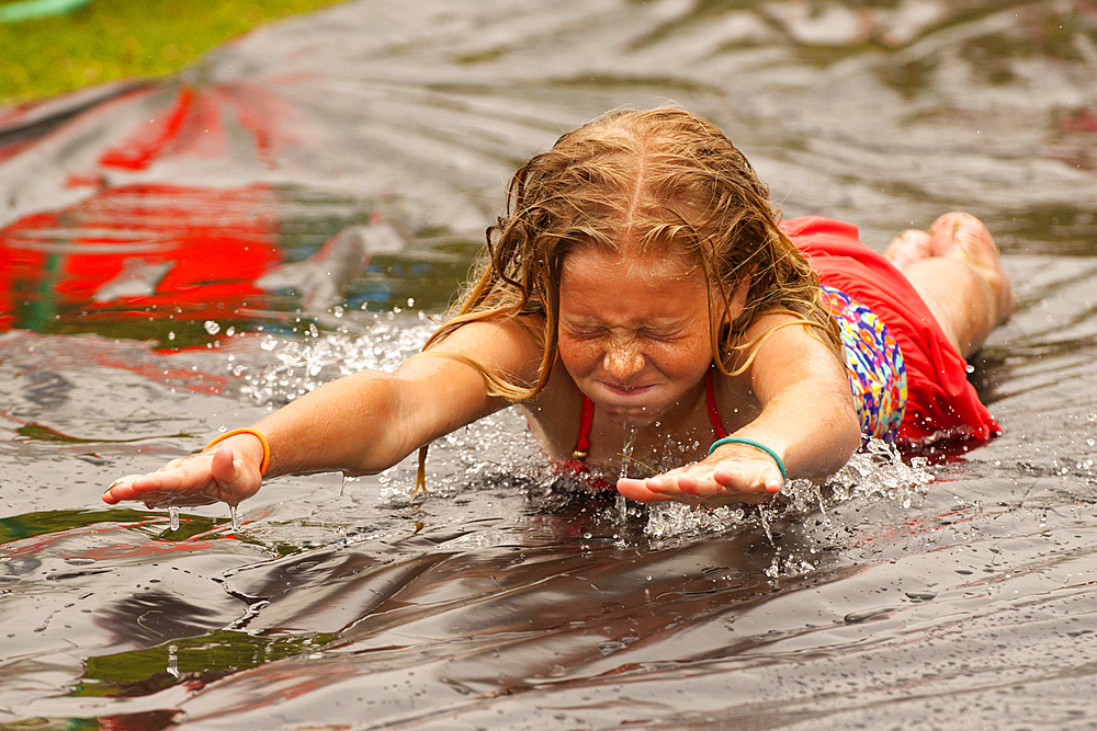 Caucasian girl sliding in water on outdoor plastic tarp