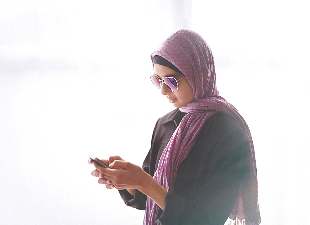 Mixed Race girl wearing heart-shape sunglasses and headscarf texting