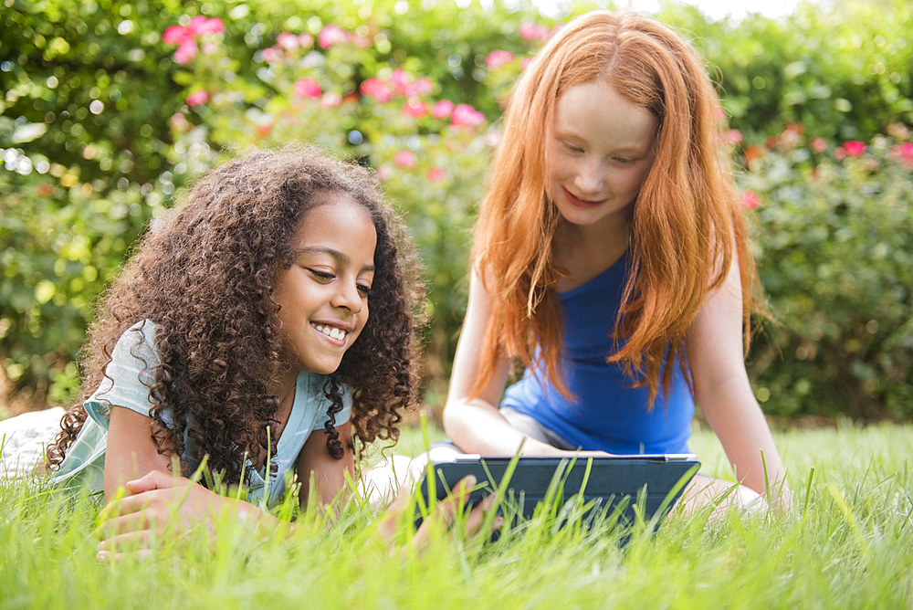 Smiling girls in grass field using digital tablet