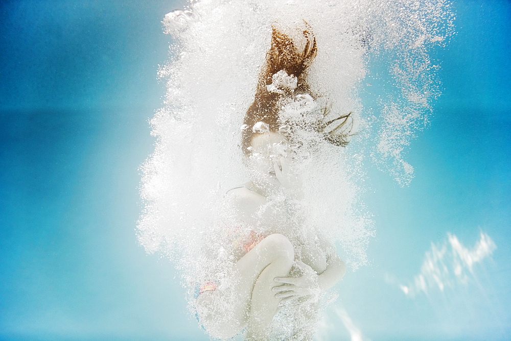 Caucasian girl swimming underwater holding nose