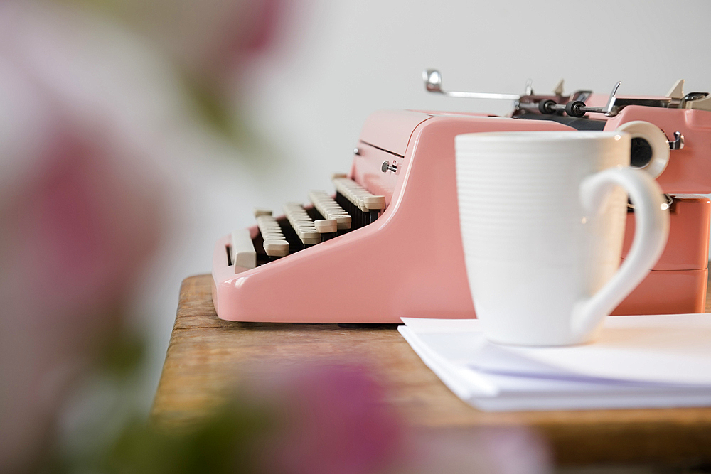 Coffee cup on pile of paper near pink typewriter