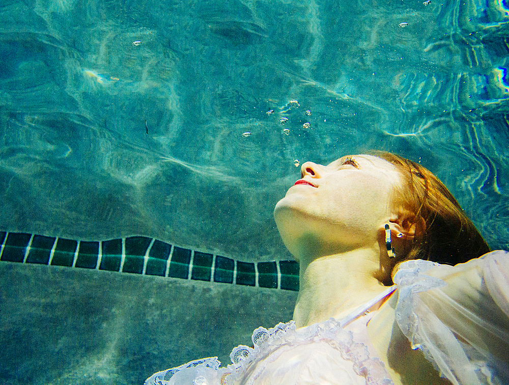 Caucasian woman wearing dress swimming underwater