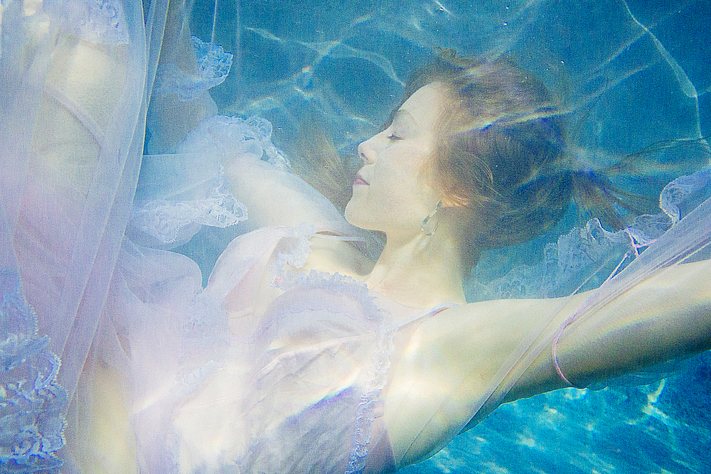 Caucasian woman wearing dress swimming underwater