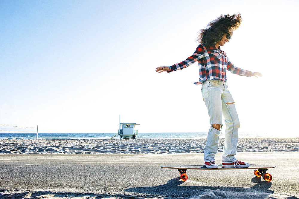 Hispanic woman riding skateboard at beach