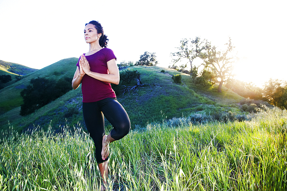 Mixed Race woman practicing yoga on hill