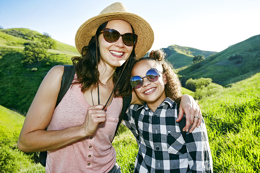 Smiling mother and daughter wearing sunglasses on hill