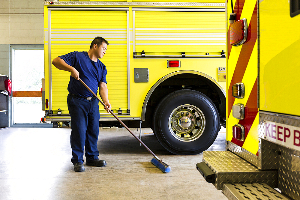 Chinese fireman sweeping floor near fire trucks