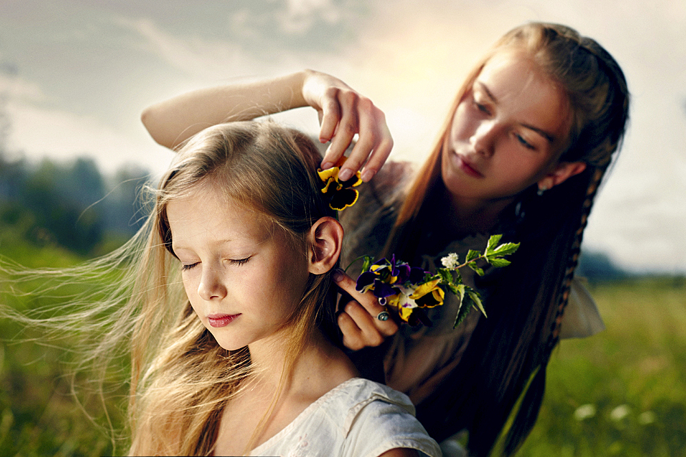 Caucasian girl placing flower in hair of sister