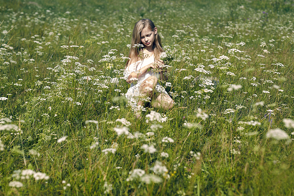 Caucasian girl crouching in field picking wildflowers