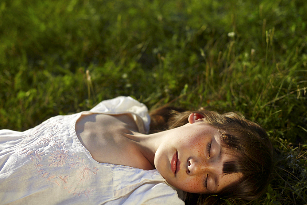 Caucasian girl laying in grass with eyes closed