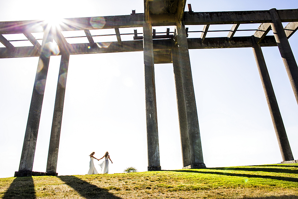 Caucasian brides holding hands walking under concrete structure