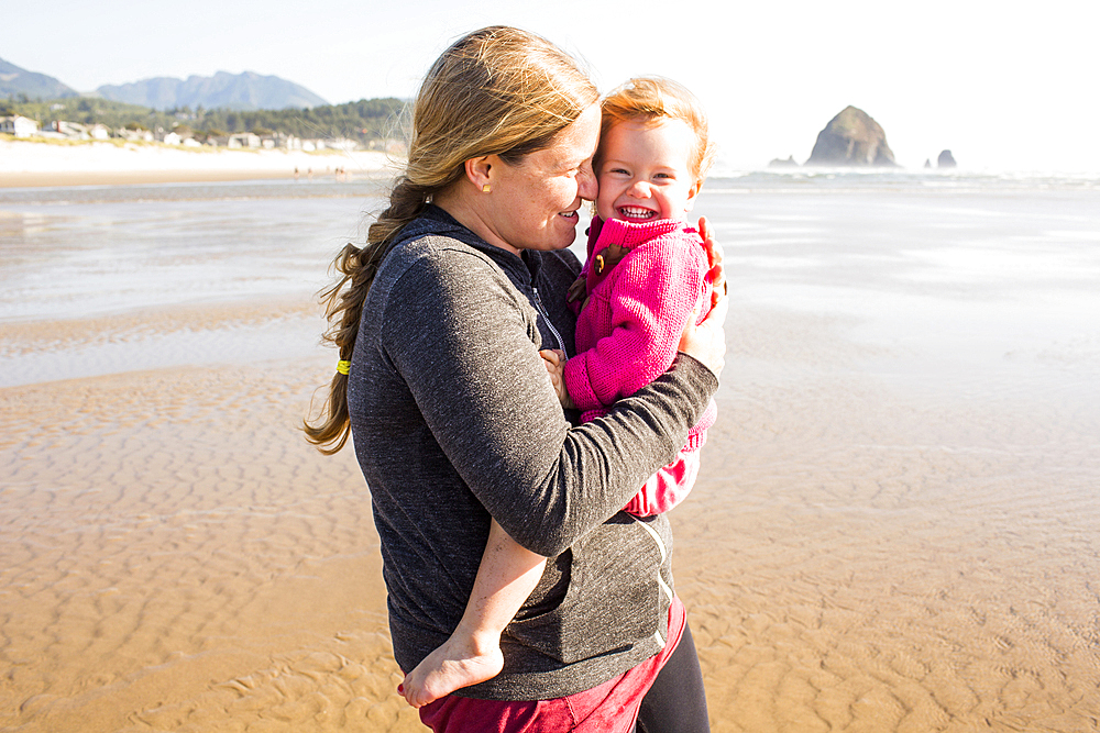 Caucasian mother carrying daughter on beach