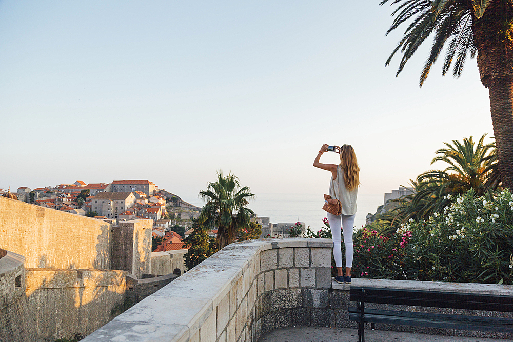 Caucasian woman standing on park wall photographing cityscape