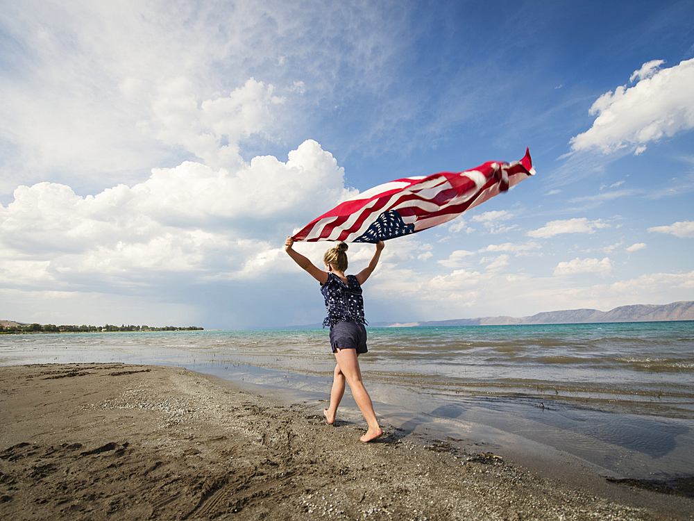 Caucasian girl walking with American flag at beach