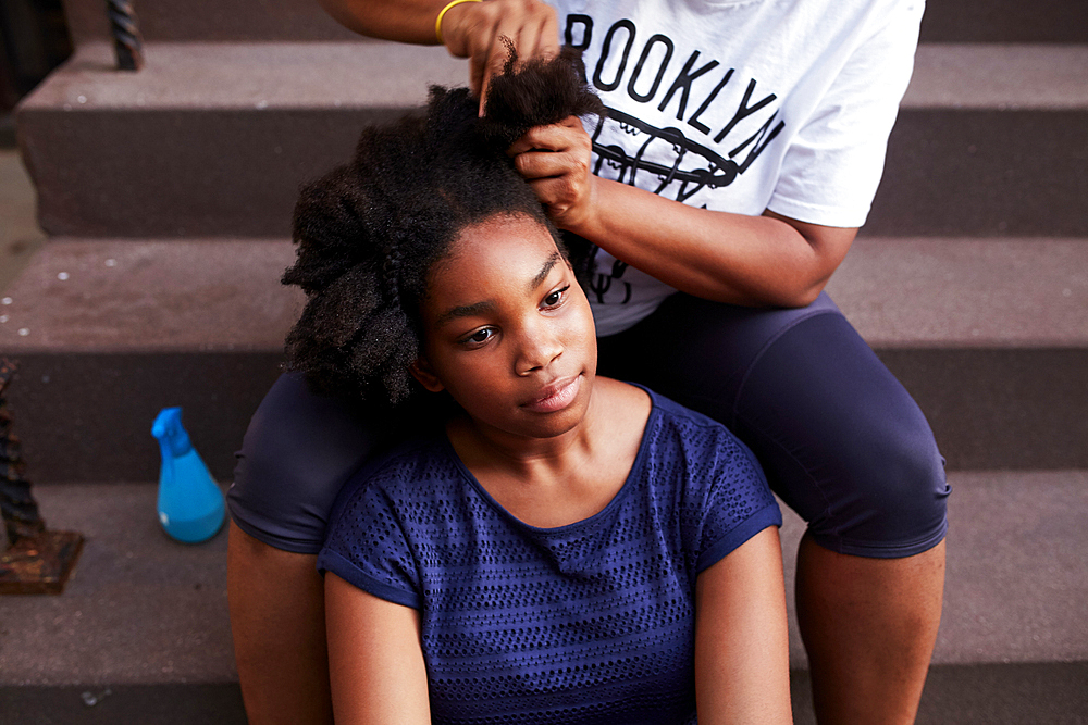 Black mother styling hair of daughter on staircase