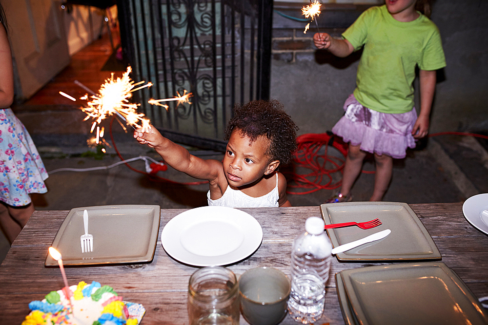 Serious girl holding burning sparkler at backyard party