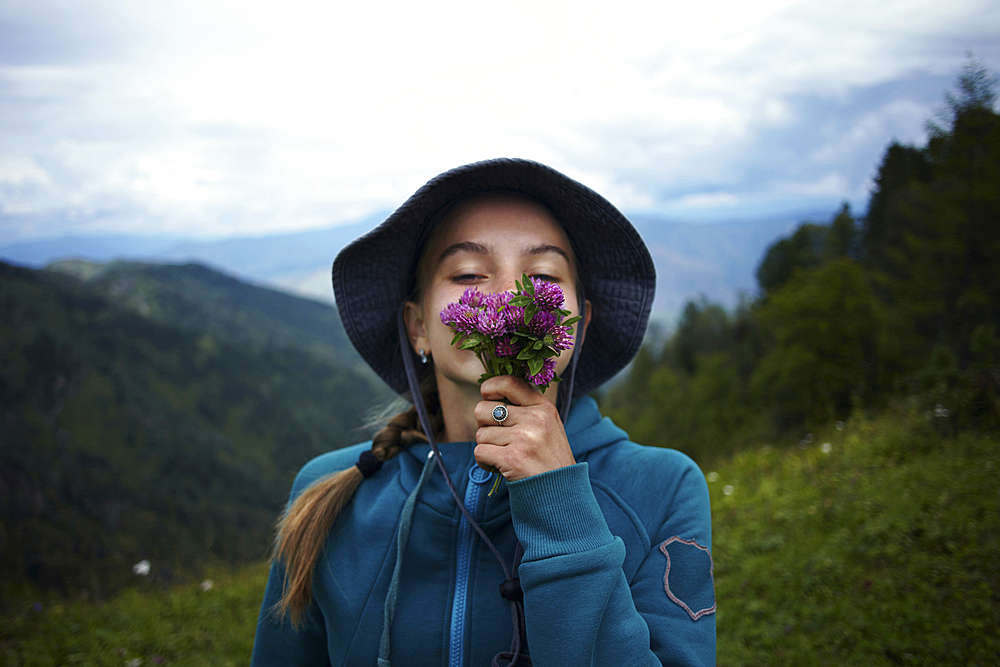 Caucasian girl smelling flowers on mountain range