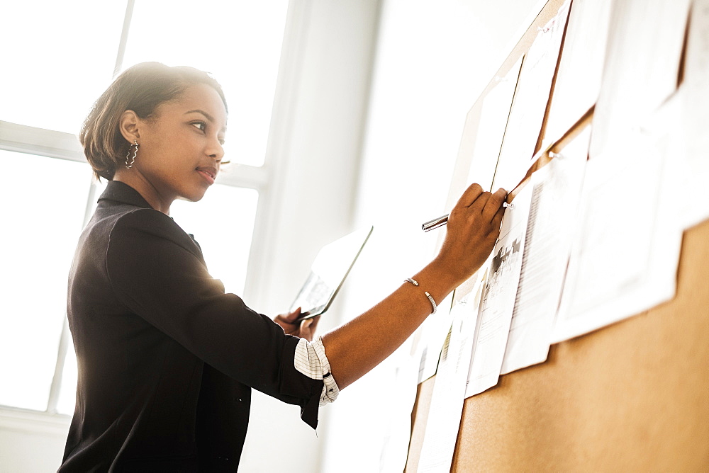 Black businesswoman using digital tablet writing on paperwork