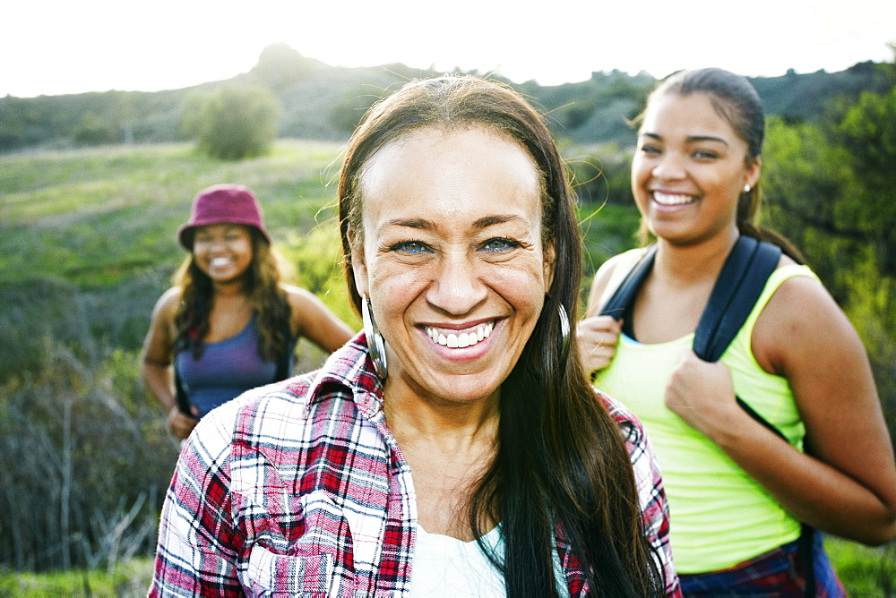 Mixed Race mother and daughters backpacking in field