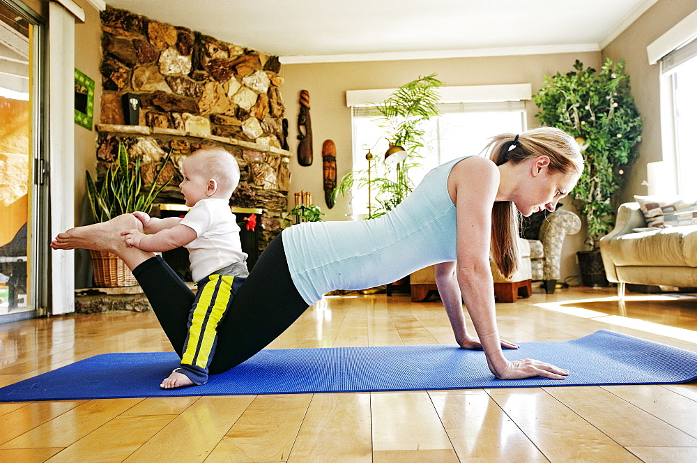 Mother working out on exercise mat with baby on legs