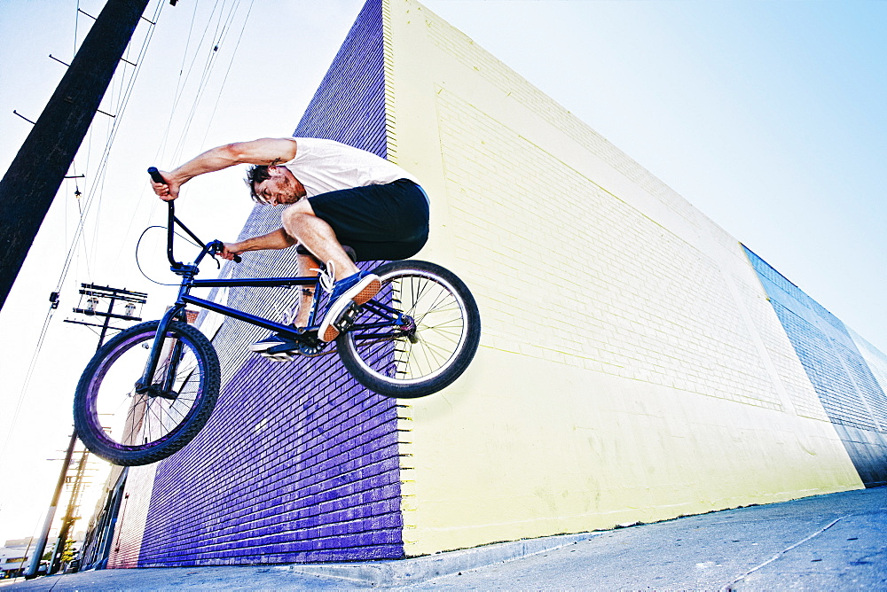 Caucasian man jumping on BMX bike on sidewalk