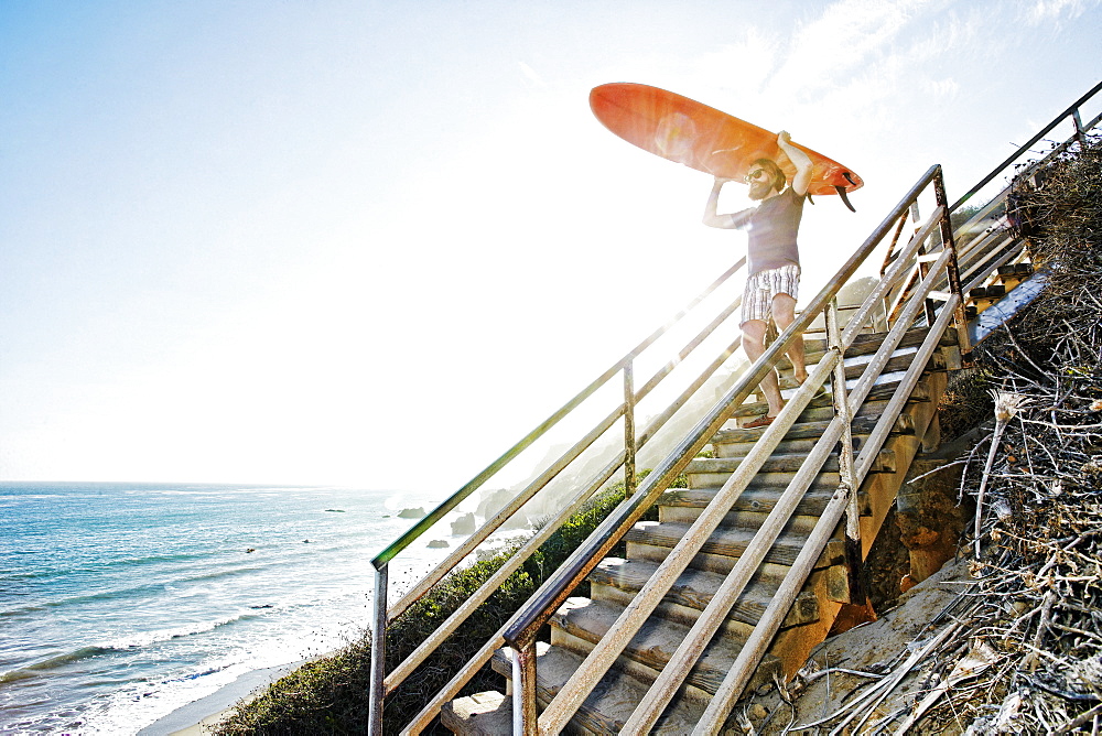 Caucasian man carrying surfboard on stairs at beach