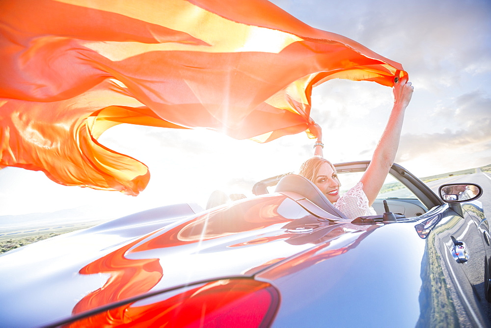 Caucasian woman holding orange fabric in wind in sports car