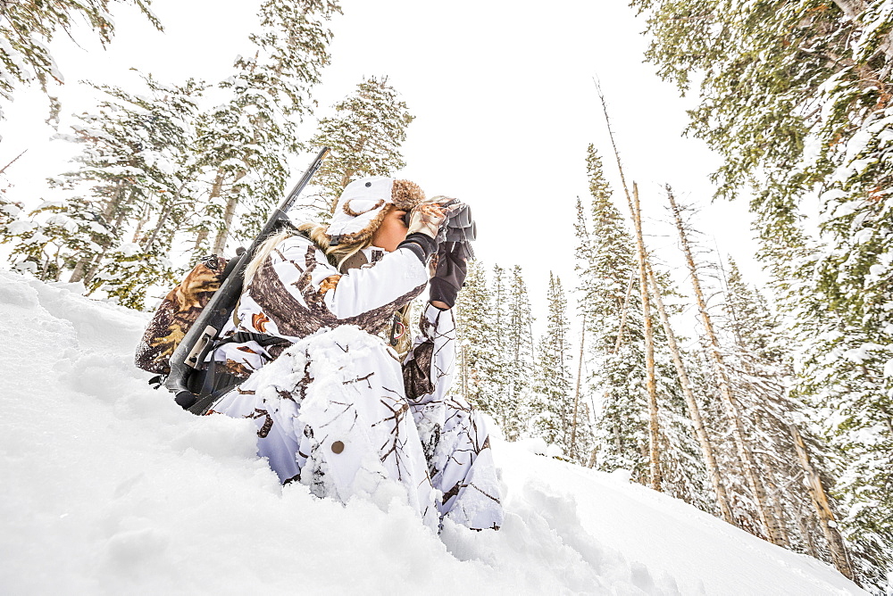 Caucasian woman hunting in forest using binoculars