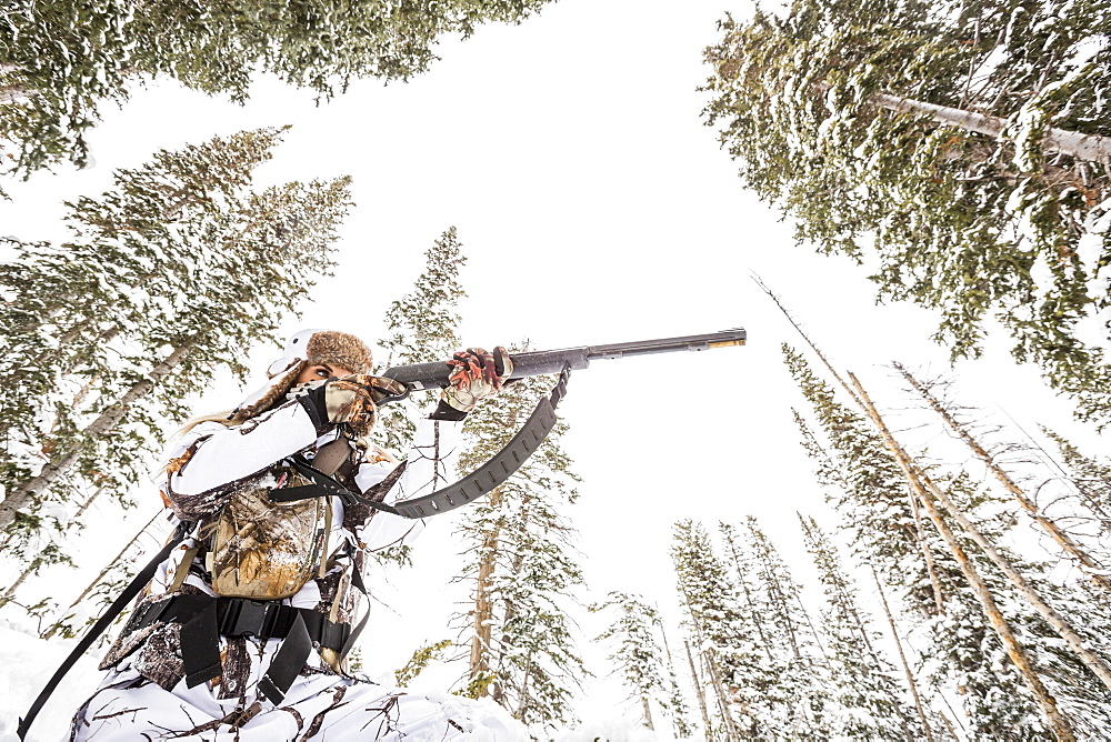 Caucasian woman hunting in forest aiming rifle