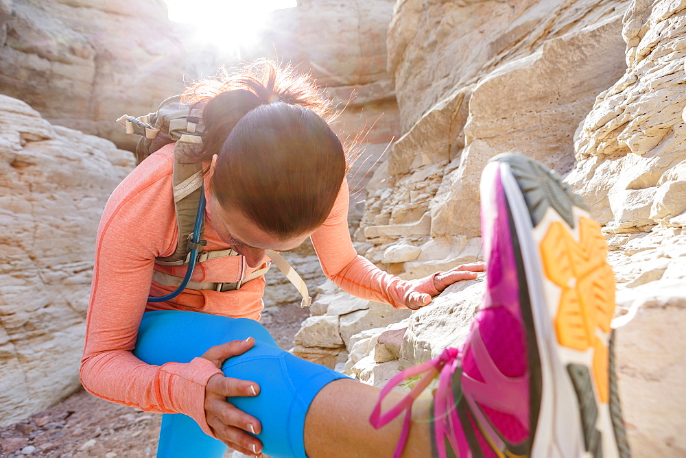 Woman stretching leg in canyon wearing backpack