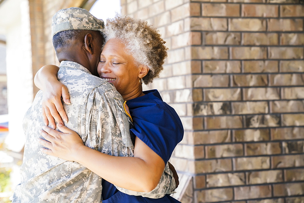 Black soldier hugging wife on front stoop