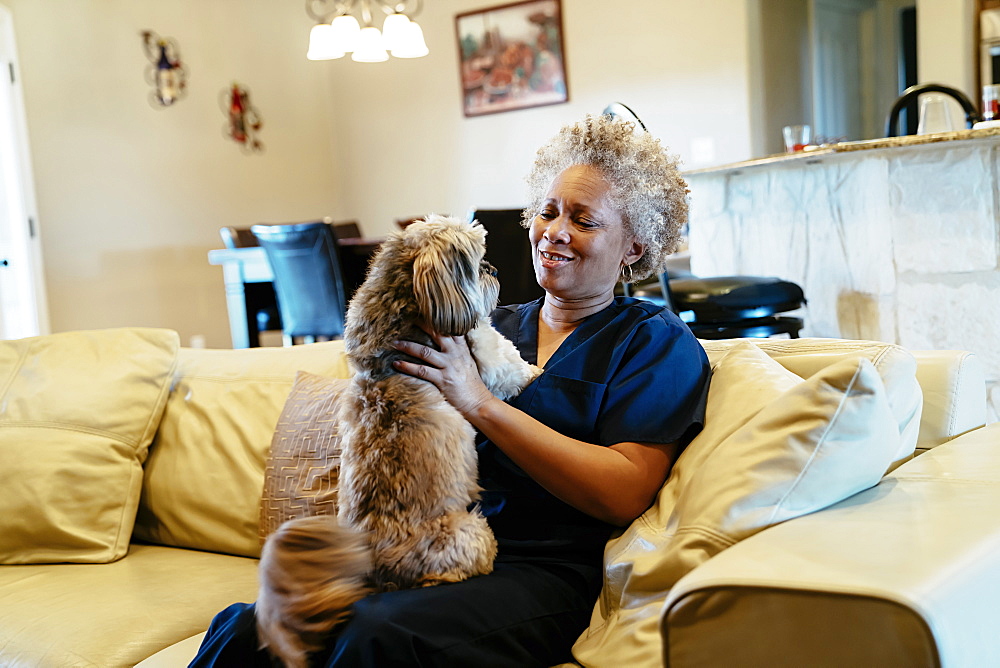 Black woman sitting on sofa playing with dog