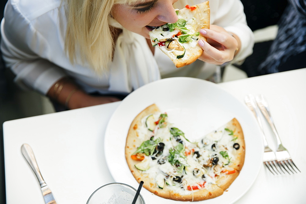 Caucasian woman eating slice of pizza in restaurant