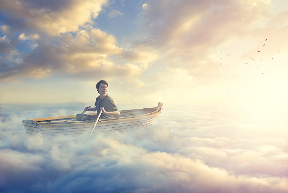 Caucasian boy paddling rowboat in clouds