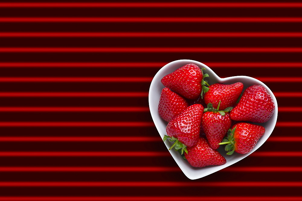 Strawberries in heart-shape bowl on red striped background