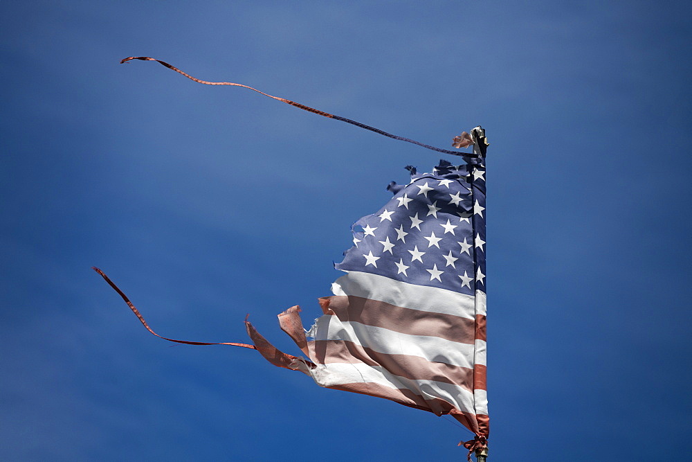 Worn and wind-torn American flag blowing against blue sky