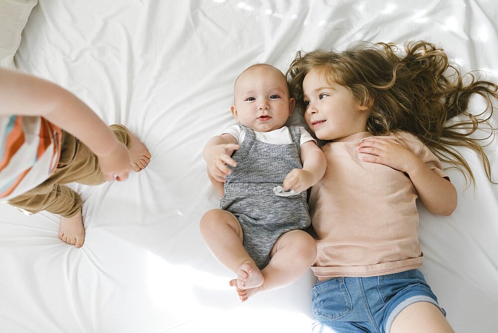 Siblings (6-11 months, 2-3) lying on bed