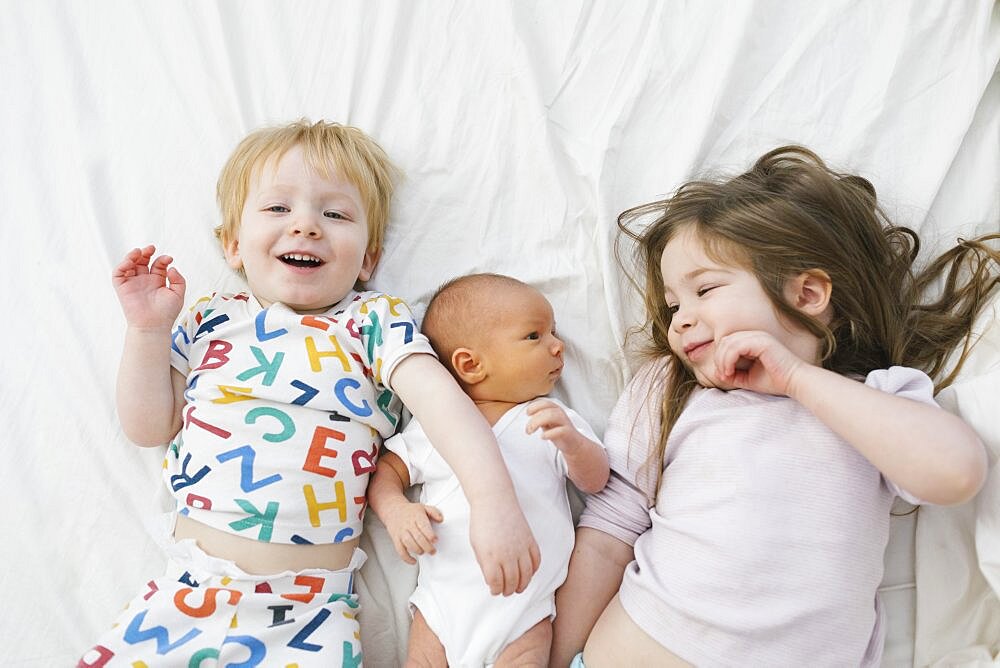 Siblings (0-1 months, 2-3) lying on bed