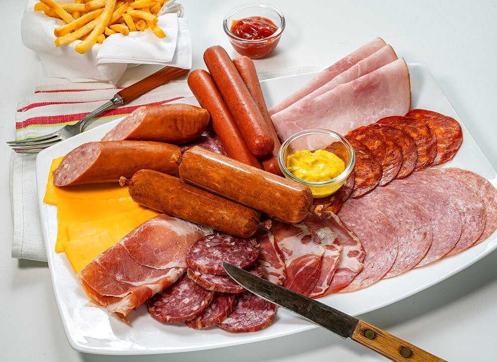 Assorted cold cuts, sausages and cheese with mustard and french fries in table setting