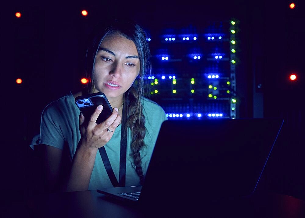 Female technician using laptop and smart phone in server room