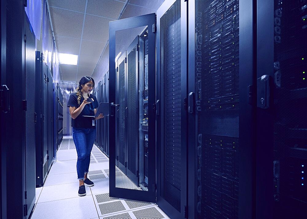 Female technician using smart phone and laptop in server room