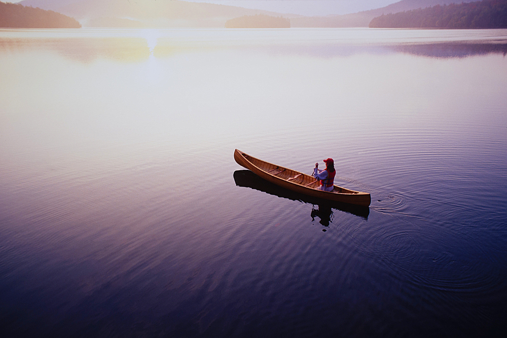 High angle view of woman paddling canoe on Lake Placid at sunrise, Adirondacks State Park