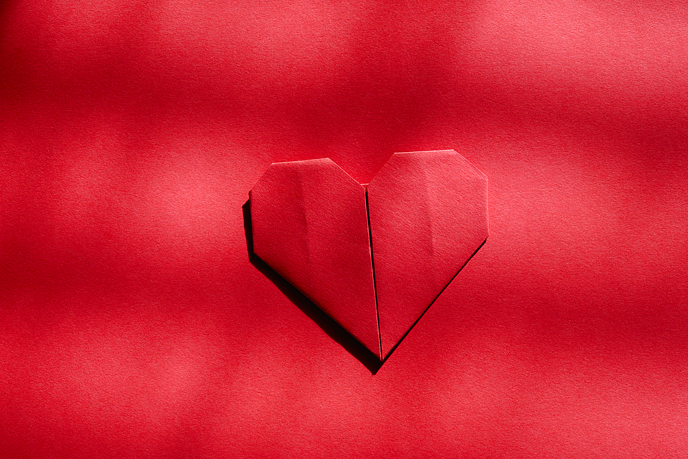 Red origami heart on red background 